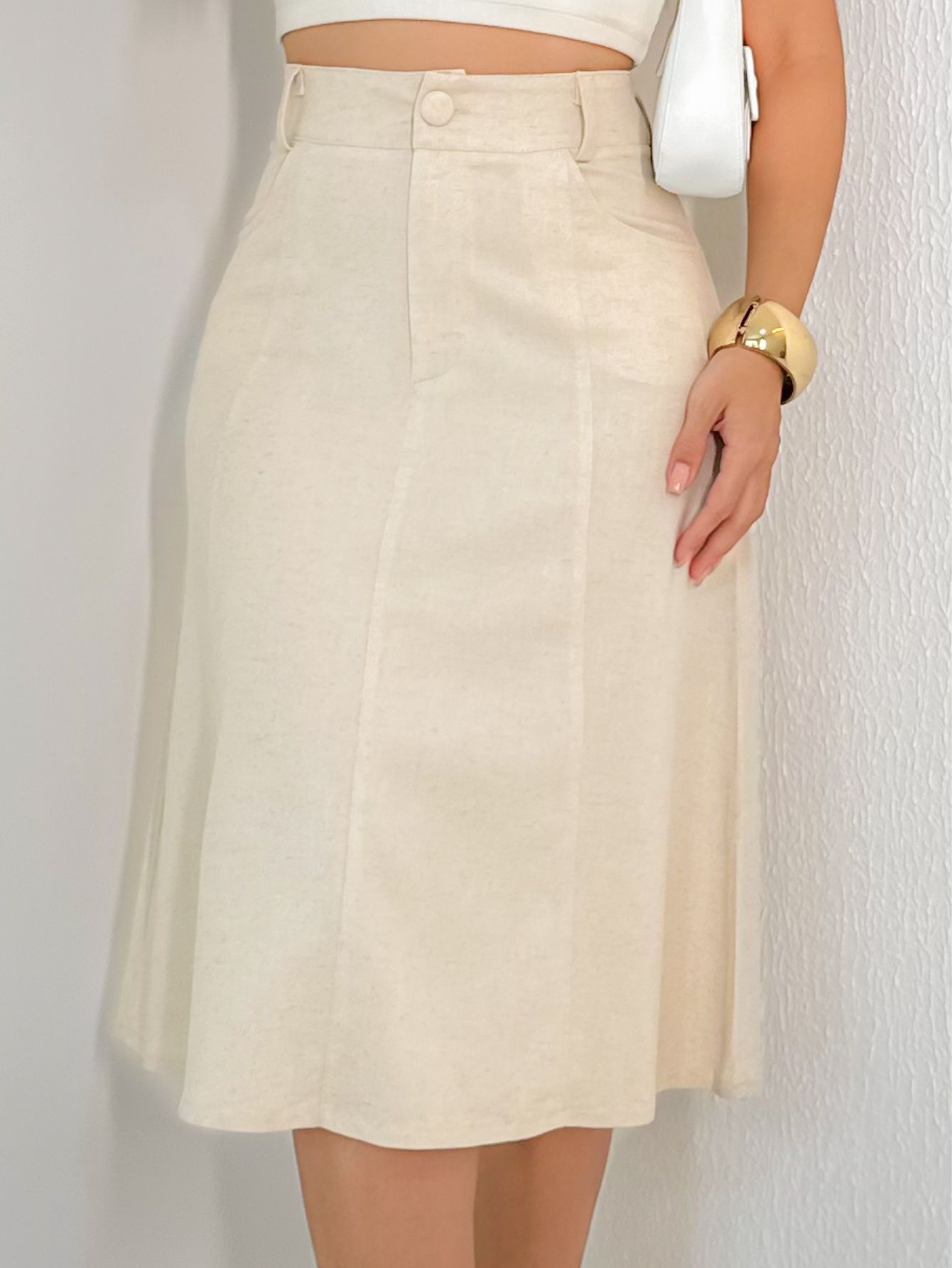 Close na parte superior da saia midi de viscolinho bege mostrando o cós com botão, costuras verticais e a textura do tecido.
