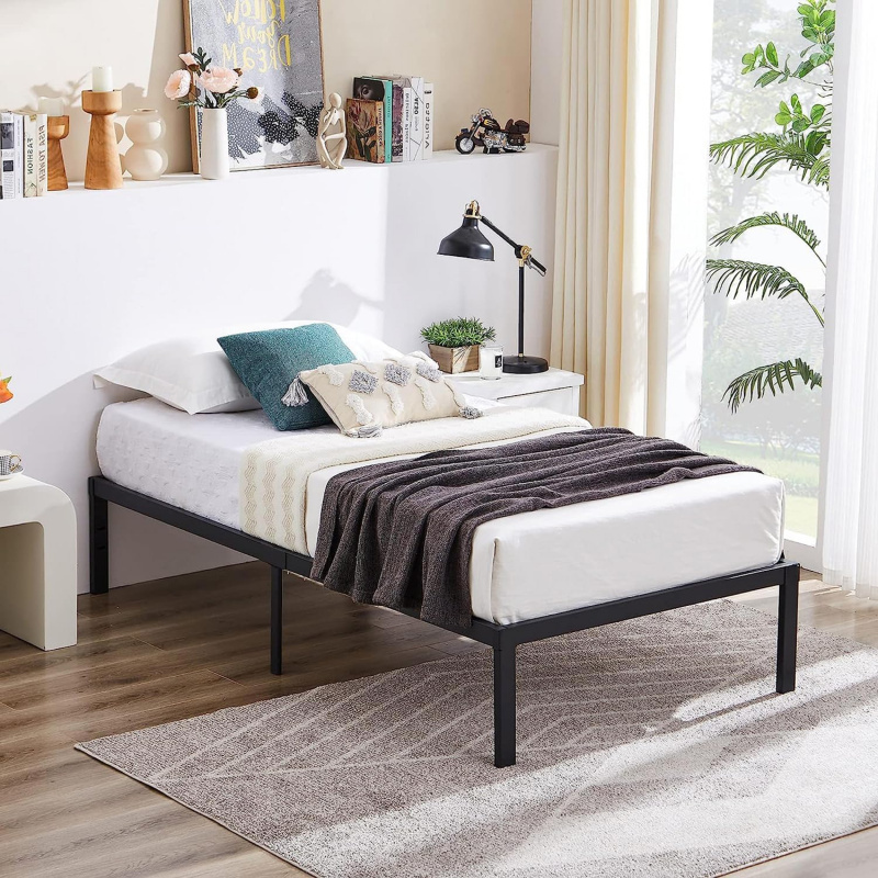 Estrutura de cama de solteiro KODI em metal preto, montada com colchão branco, travesseiros azuis e brancos, e uma manta cinza, ambientada em um quarto moderno com mesa de cabeceira e decoração.