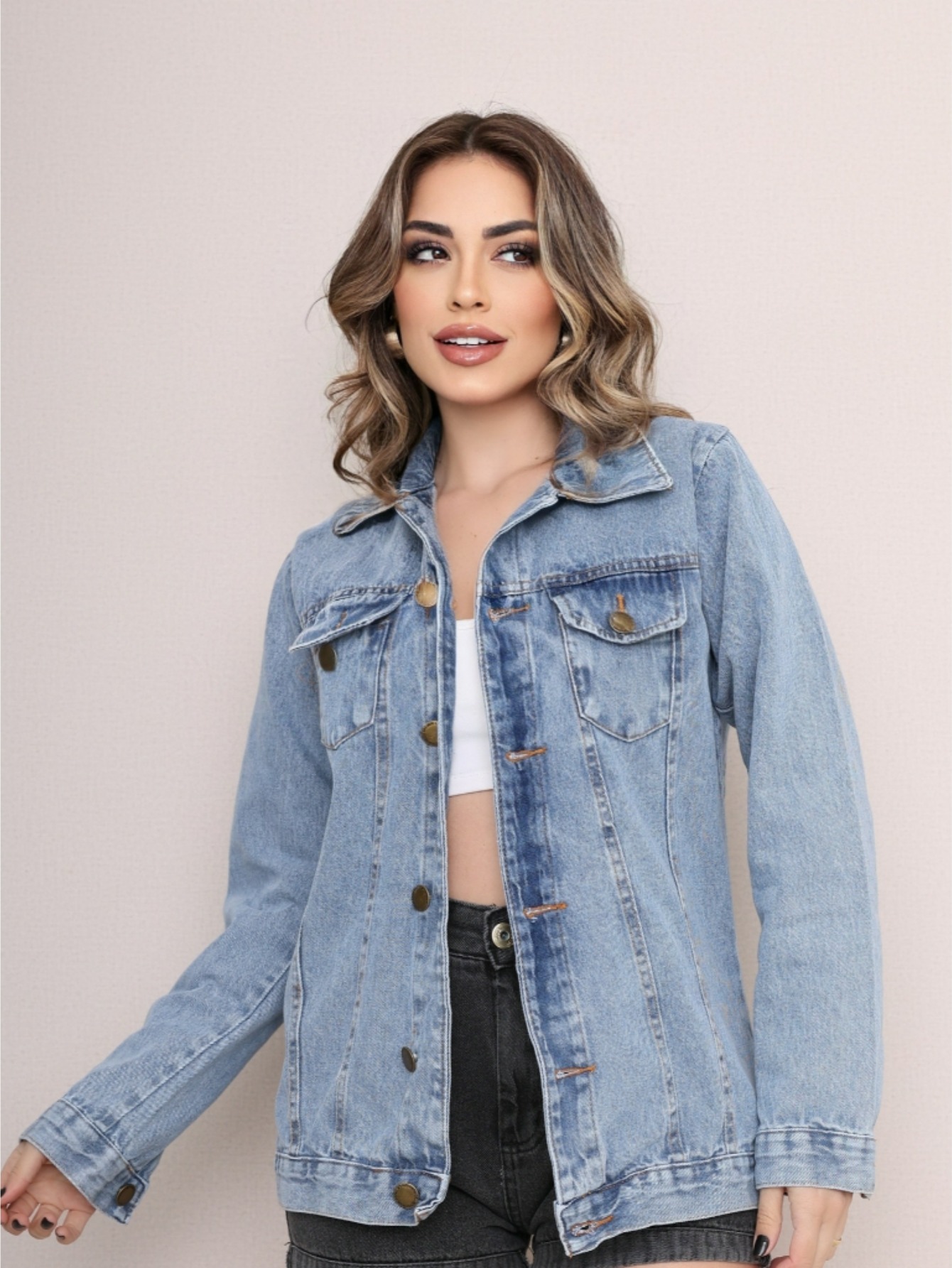 Mulher vestindo jaqueta jeans clara de manga longa com botões metálicos e bolsos frontais sobre top branco.