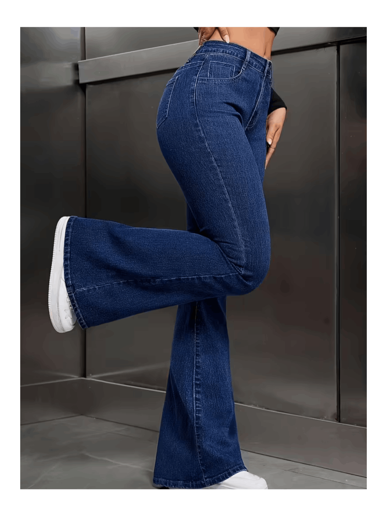 Vista lateral da calça flare jeans plus size com modelo em pé de lado mostrando o corte da perna