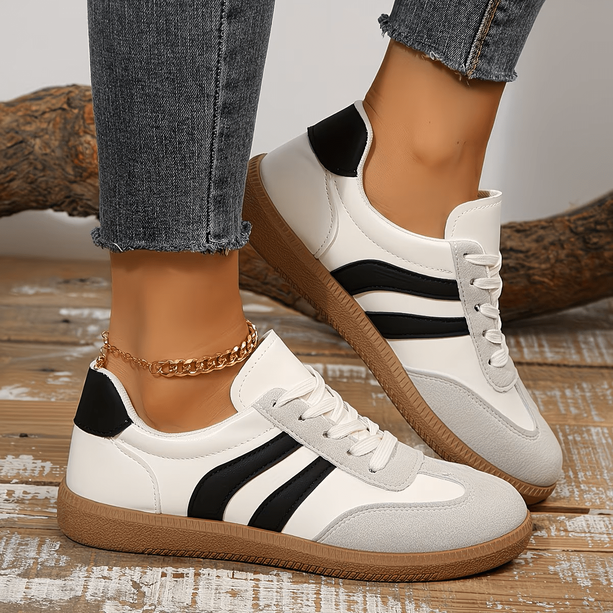 Close-up de um par de tênis femininos brancos com detalhes em preto e cinza, e sola marrom, usados por uma pessoa com jeans.