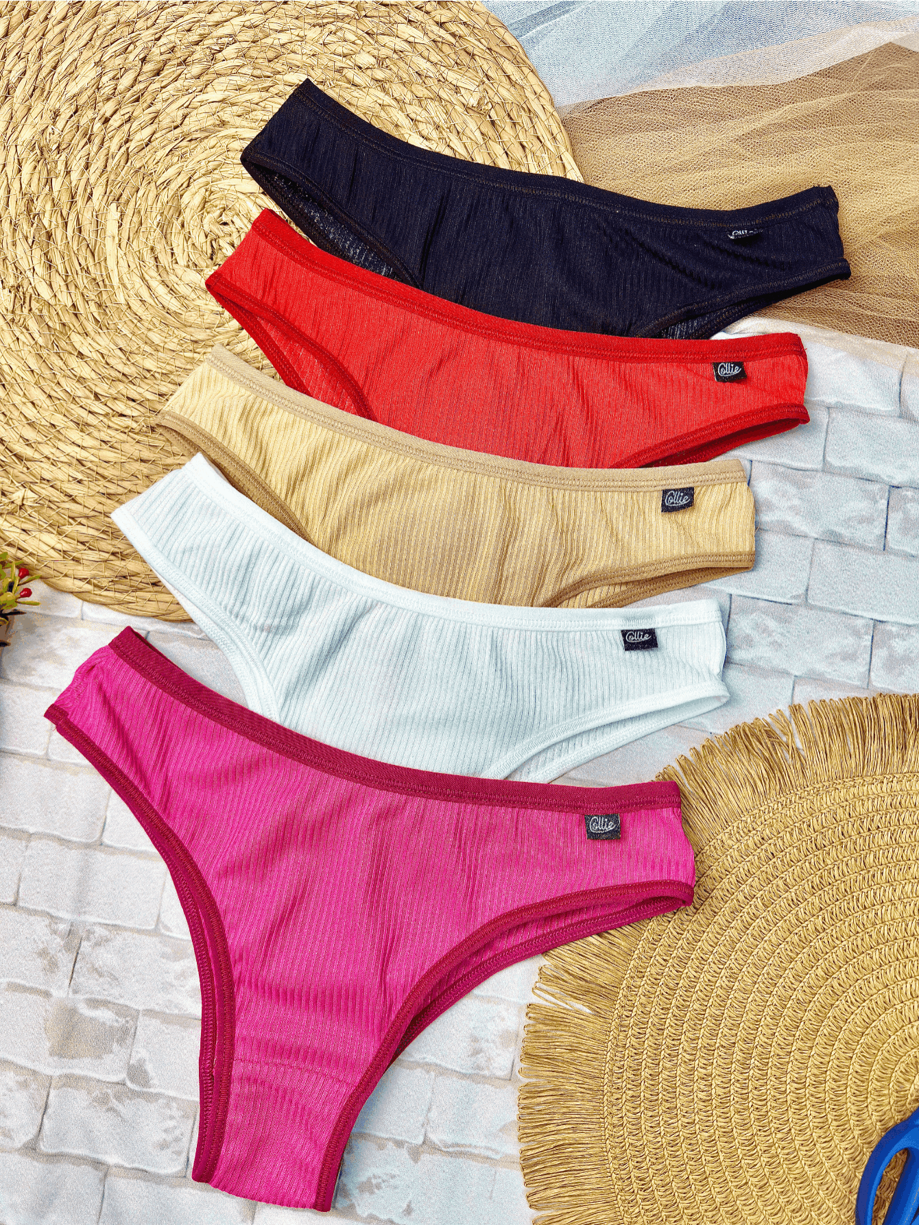 Kit de cinco calcinhas tanga em cores variadas dispostas sobre base de palha e piso de tijolinhos