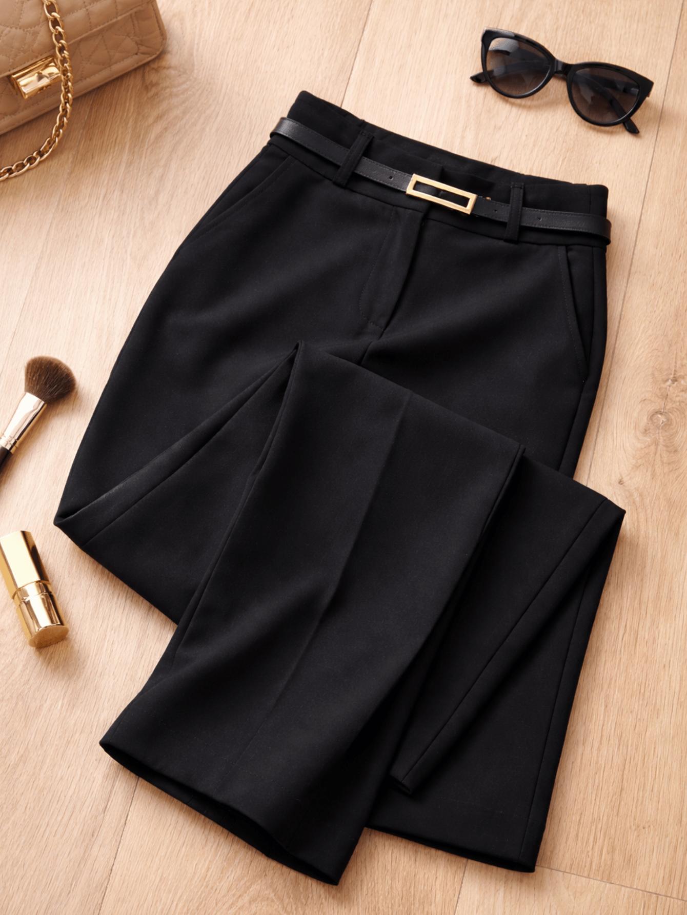 Calça pantalona preta de alfaiataria dobrada sobre superfície de madeira com cinto, óculos escuros, pincel de maquiagem e batom ao lado