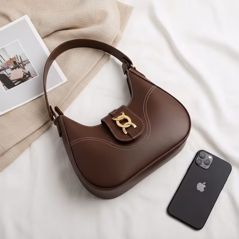 Bolsa baguete feminina marrom com textura e fecho dourado ao lado de um smartphone