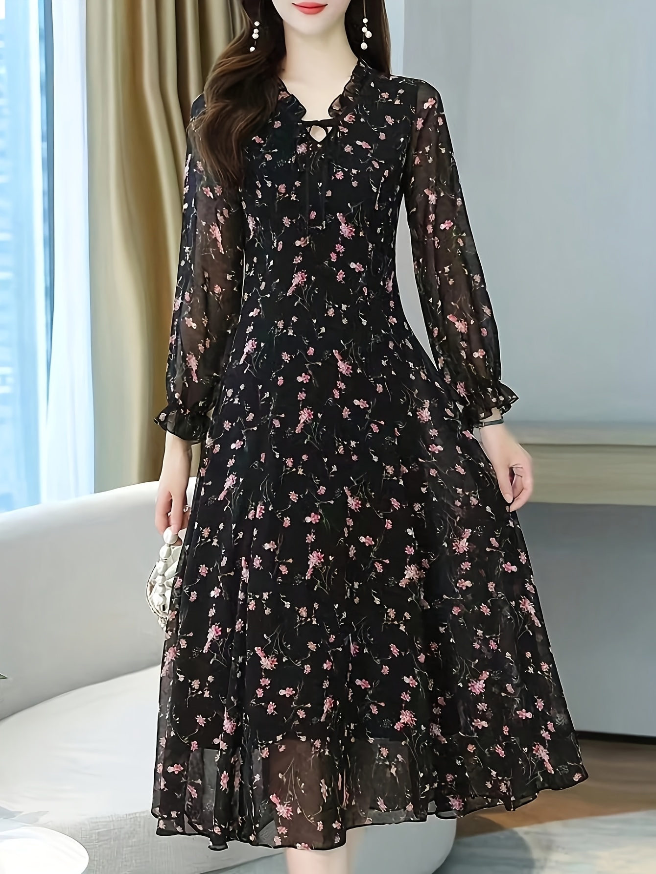 A model wearing a black maxi dress with a delicate floral print posing against a bright background