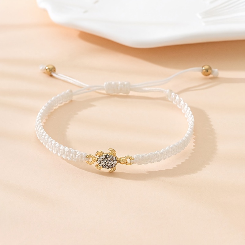 A Minimalist Couple's Metal Bracelet With Gemstones, Featuring A Turtle Design And Braided Cord