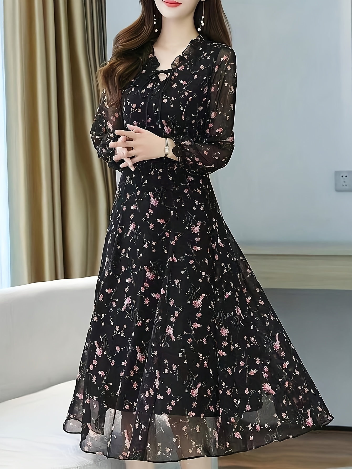 A model wearing a black maxi dress with a delicate floral print posing against a bright background