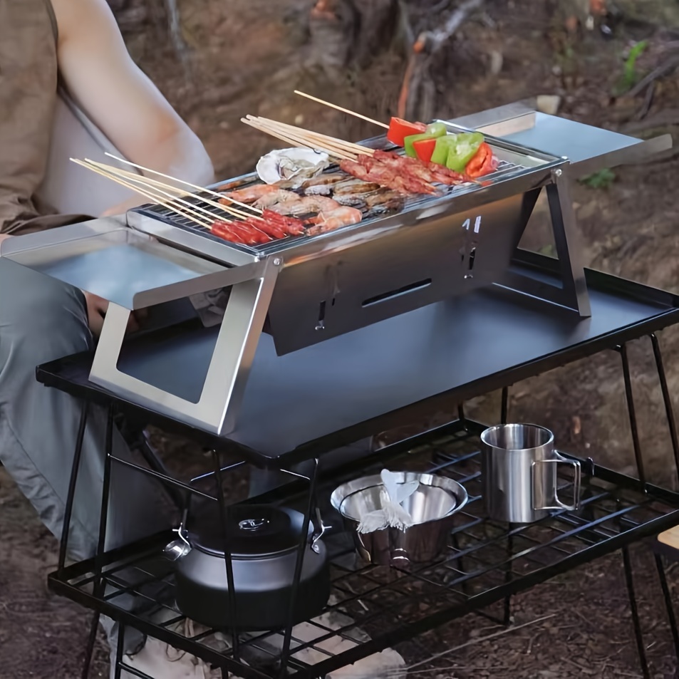 Griglia per barbecue portatile vuota calda con fuoco ardente e carbone di  legna su sfondo nero