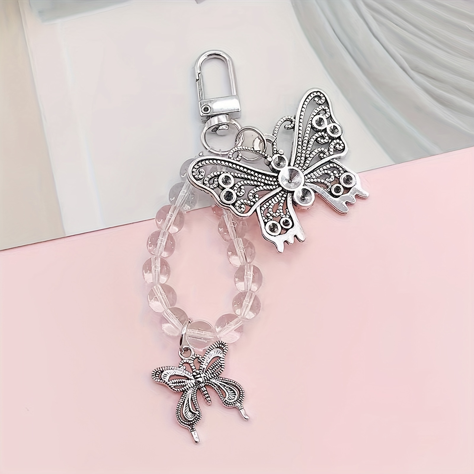 A Silvery Double Butterfly Phone Charm With Transparent Beads, Suitable For DIY Phone Case Decoration And Hanging On Keys Or Earphones.