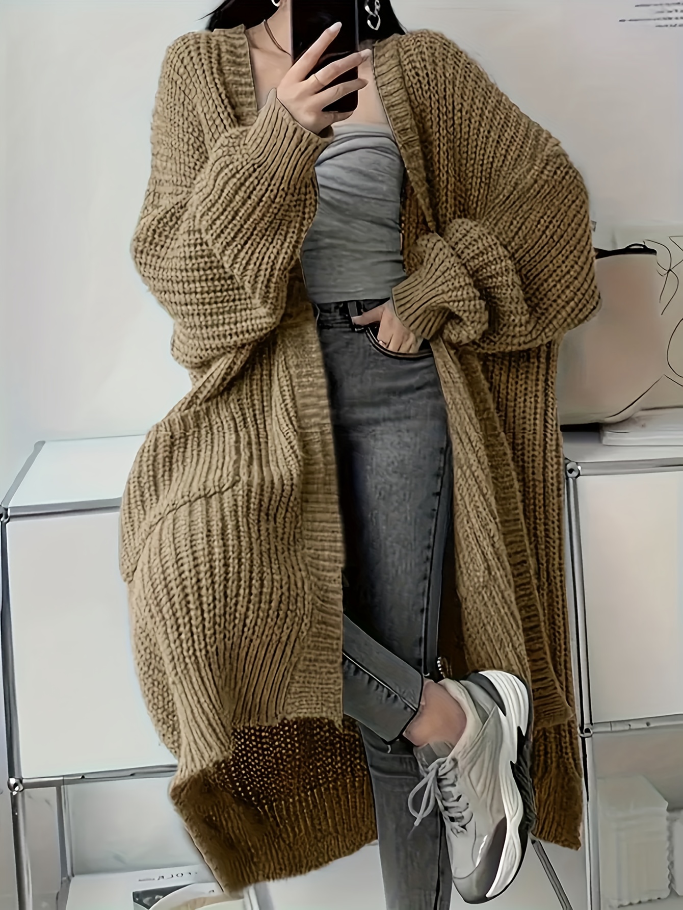A lady wearing a beige oversized knitted coat with pockets sold by 100 Spartans