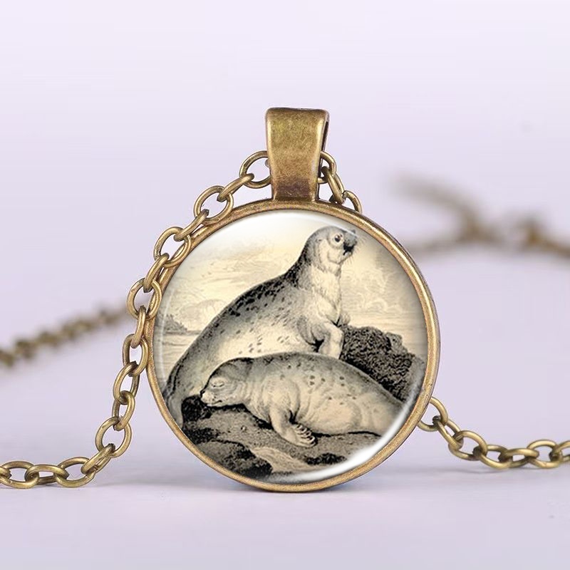 TEMU A Packaged Item ( Chain Necklace With A Brown Metal Glass Inlay Featuring Colorful Patterns), Depicting 2 Seals On A Rock, 1 Standing And Lying