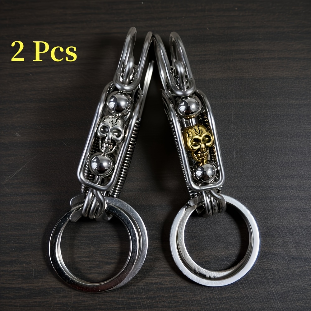 E-shop Zwei stylische Schlüsselanhänger, handgefertigt mit mehreren Schichten gebogenem Stahldraht, mit einem mattgoldenen Totenkopf in mechanischem