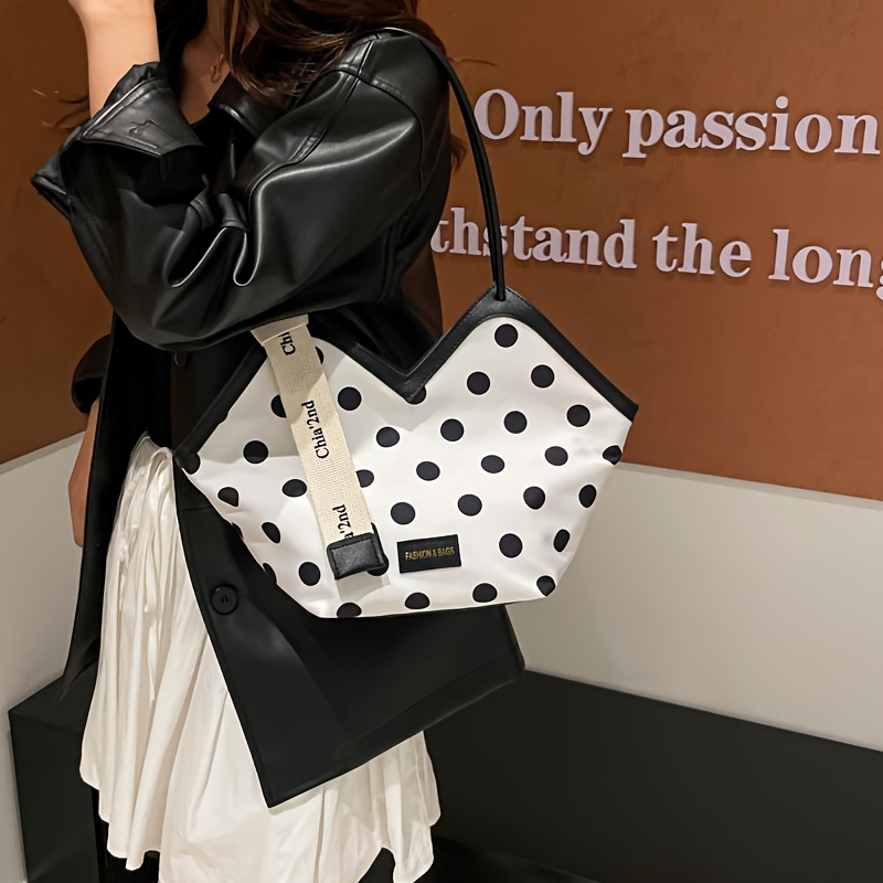 White polka dot shoulder bag with black trim and unique geometric shape, featuring branded ribbon detail
