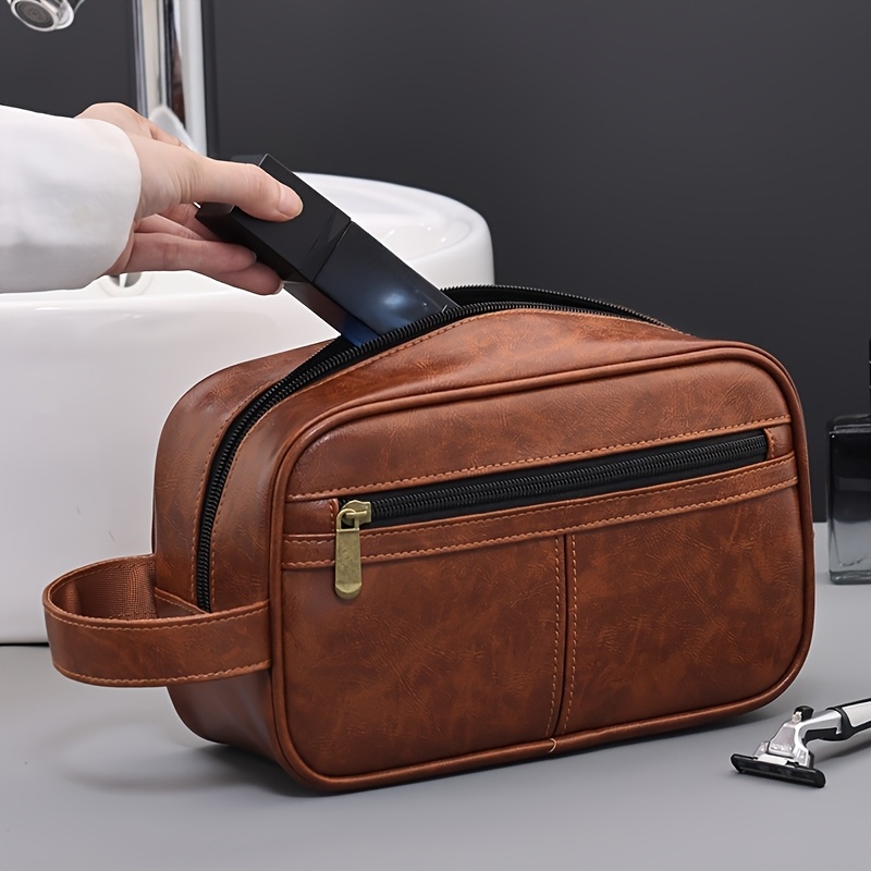 A hand putting a clipper in a brown leather toiletry bag sold by 100 Spartans.