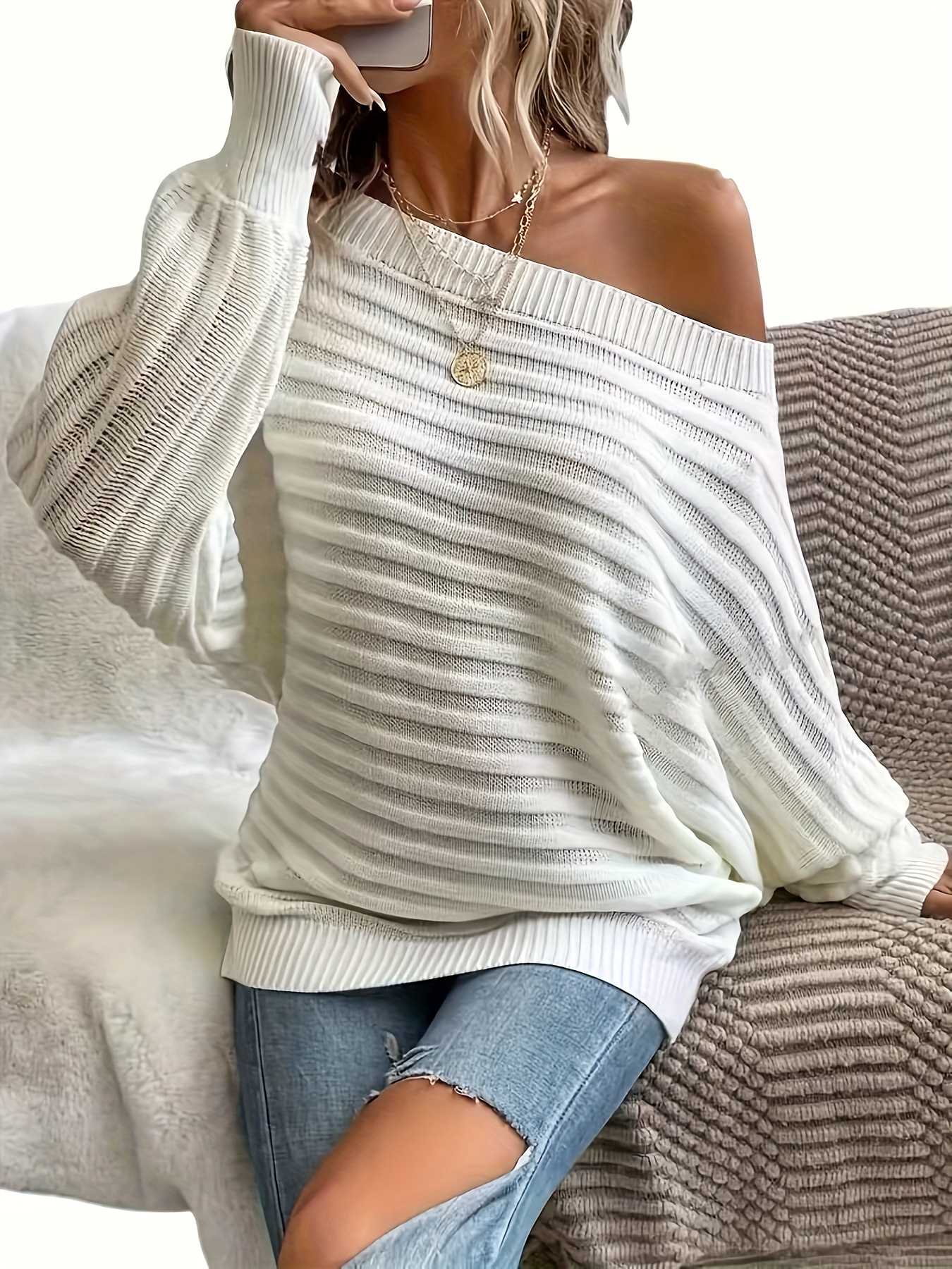 The front view of a woman wearing a beige women's off the shoulder sweater sold by 100 Spartans