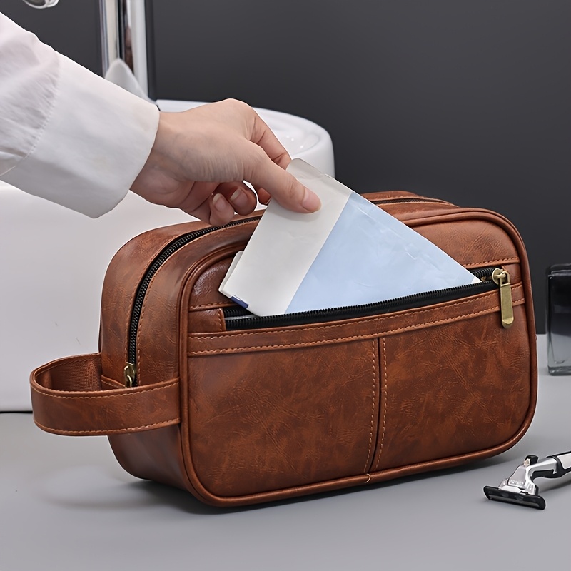 A hand putting an envelope into a brown leather toiletry bag sold by 100 Spartans.