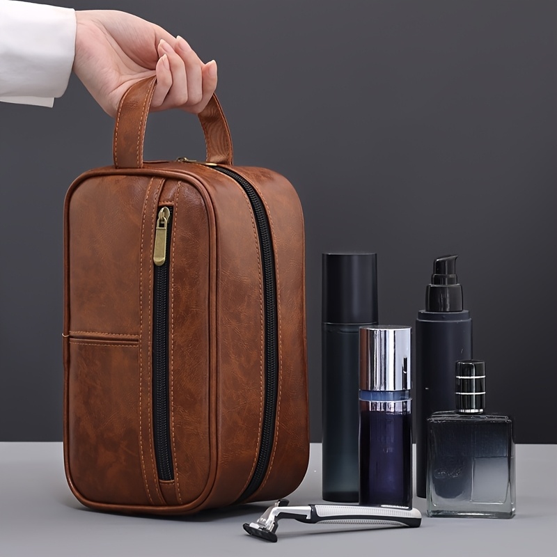 A hand holding a brown leather toiletry bag sold by 100 Spartans.