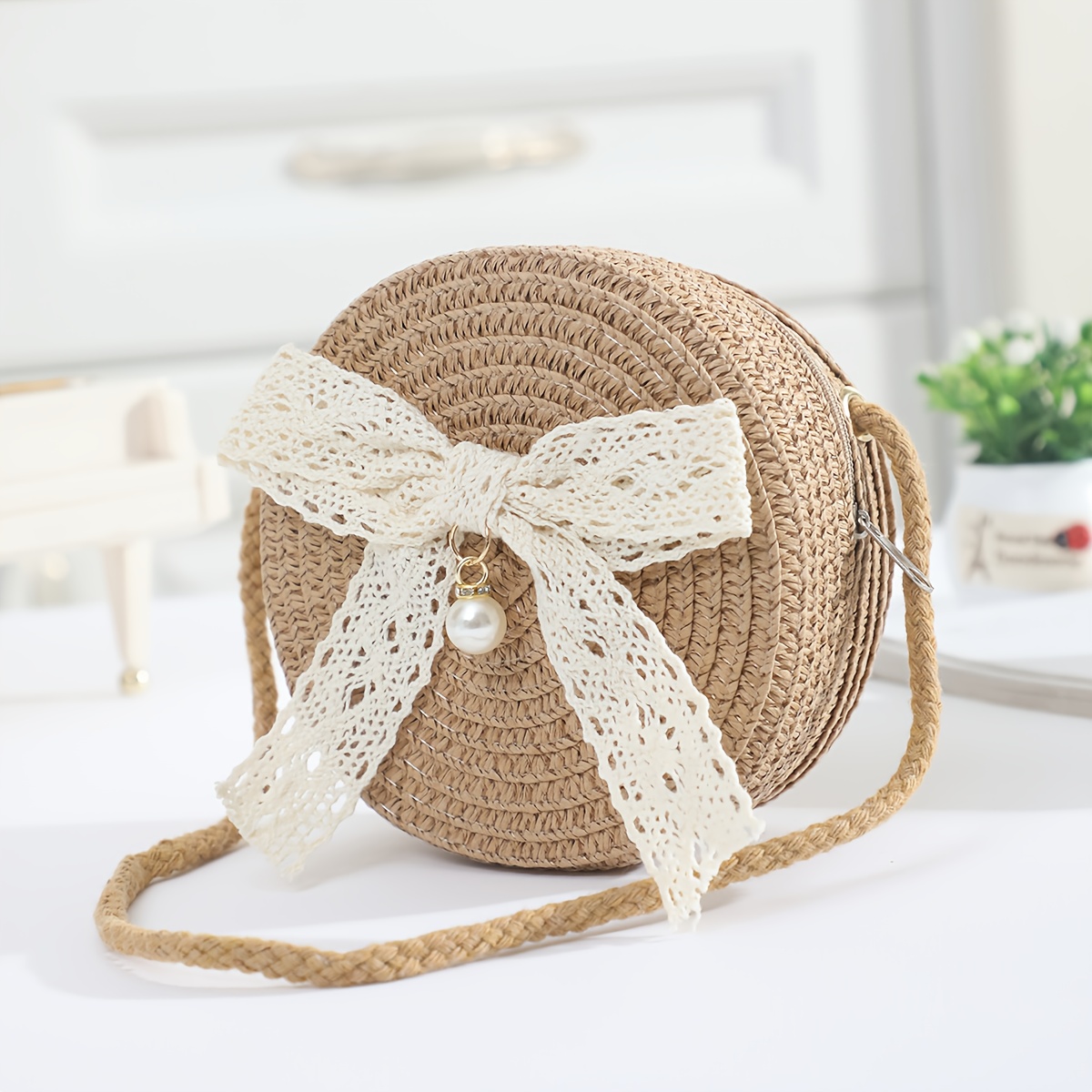 Image of A Small Round Crossbody Bag With A Lace Bow And Pearl Decoration, Featuring A Zip Closure And An Adjustable Shoulder Strap. Its Compact Size Of 12cm Makes It Suitable For Holding Keys And Snacks