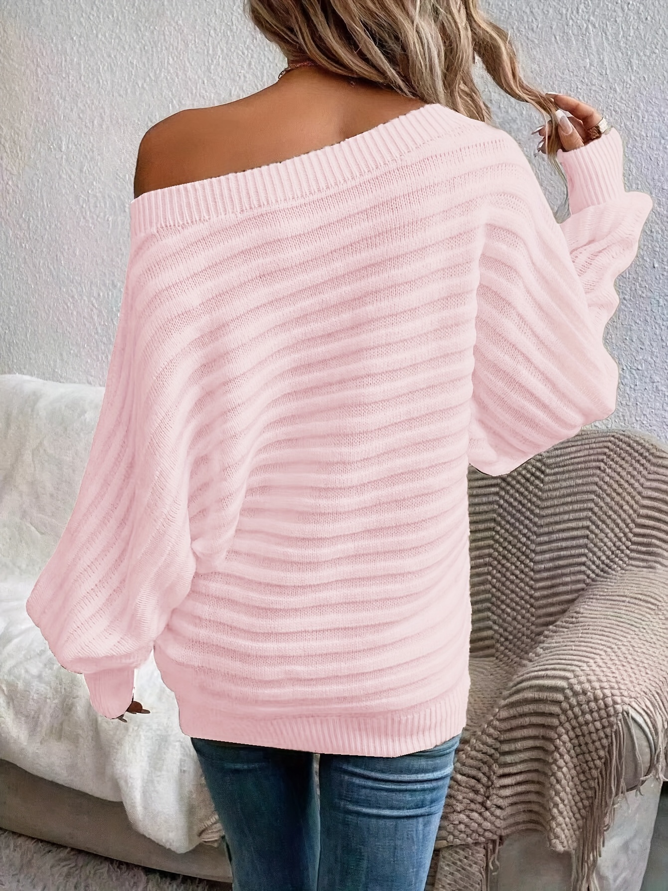 The back view of a woman wearing a pink women's off the shoulder sweater sold by 100 Spartans