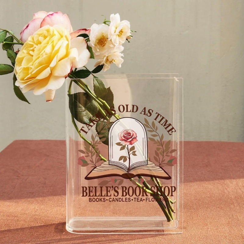 Clear book-shaped vase with a floral bookshop design holding flowers