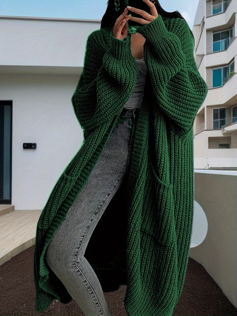 A lady wearing a green oversized knitted coat with pockets sold by 100 Spartans