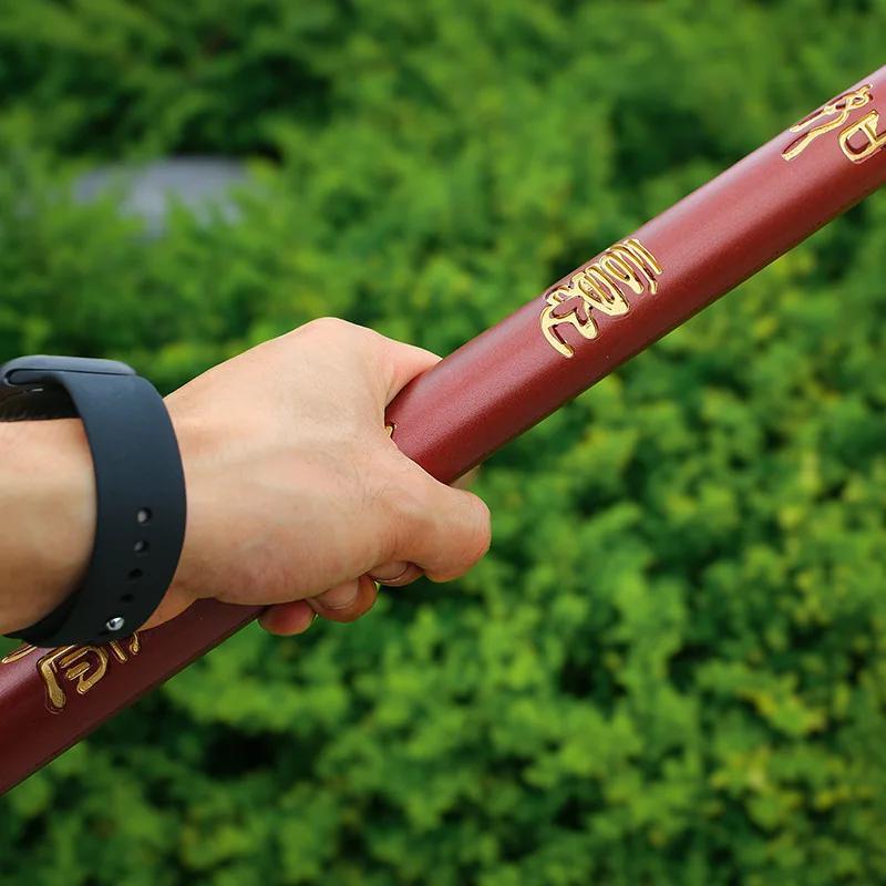Hand holding a Sun Wukong Stick  with gold text against a green blurred background