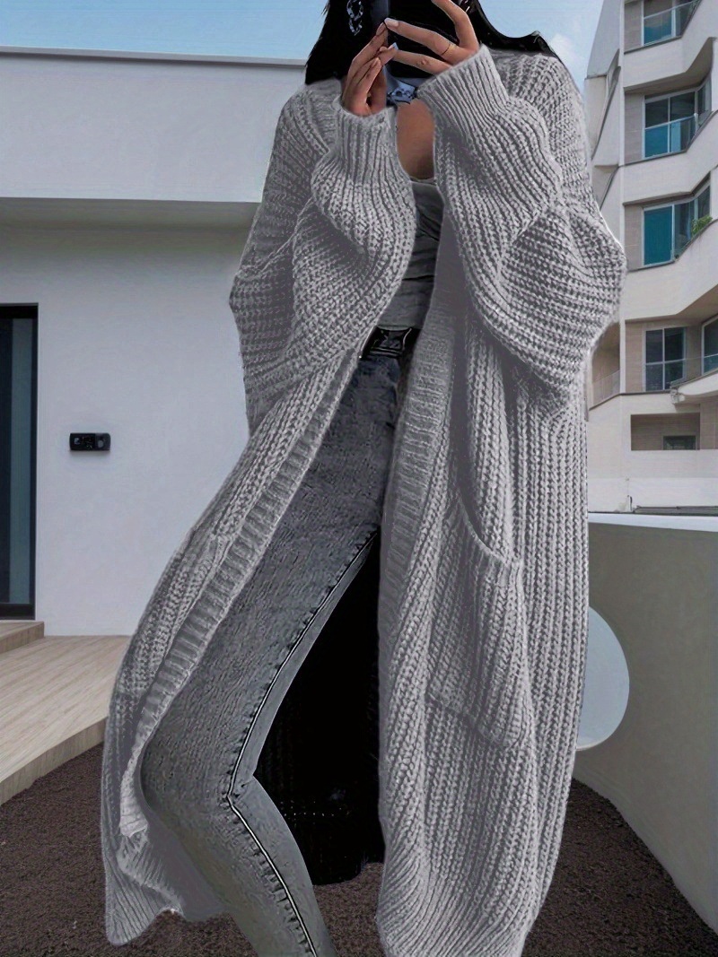 A lady wearing a light grey oversized knitted coat with pockets sold by 100 Spartans
