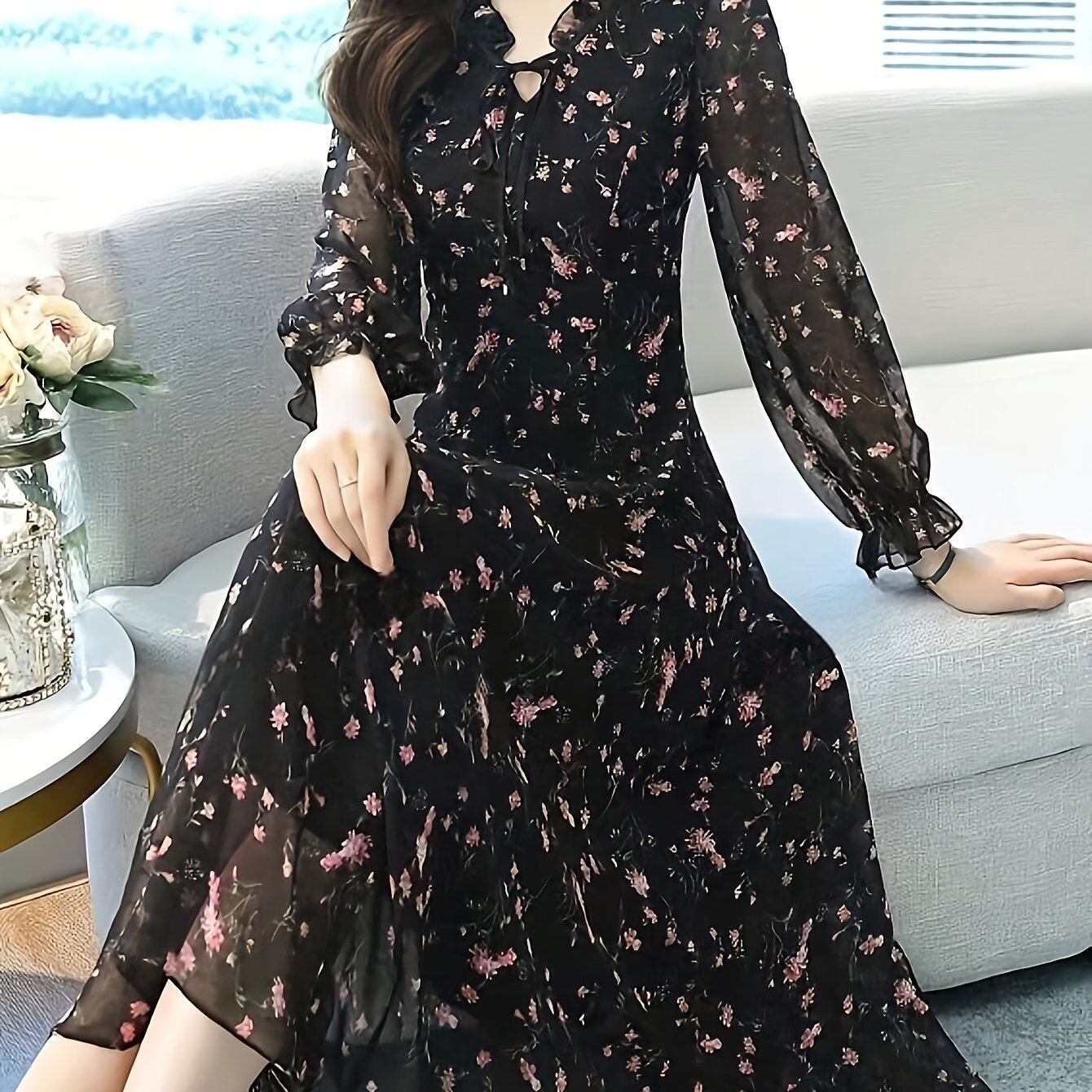 A model wearing a black maxi dress with a delicate floral print posing against a bright background